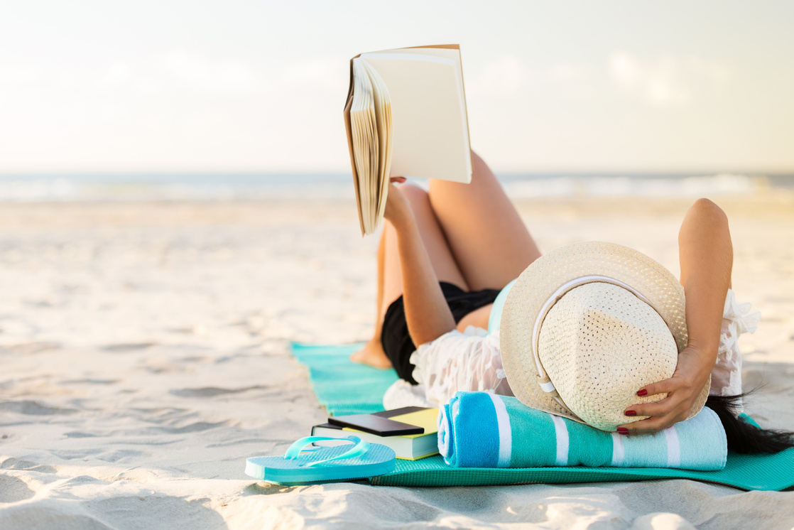 Woman lies on the beach reading a book
